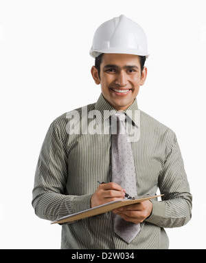 Portrait of a male engineer wearing hardhat et écrit sur un presse-papiers Banque D'Images