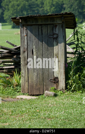 Old Wooden outhouse, faite de panneaux de bois et fer à cheval pour les charnières, dans un champ vert avec des bois en arrière-plan Banque D'Images