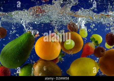 Fruits splash dans l'eau avec des bulles contre fond bleu Banque D'Images