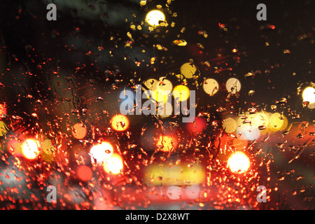 Rue et de voiture à travers les gouttes de pluie sur les pare-brise de voiture dans la nuit. England UK Banque D'Images