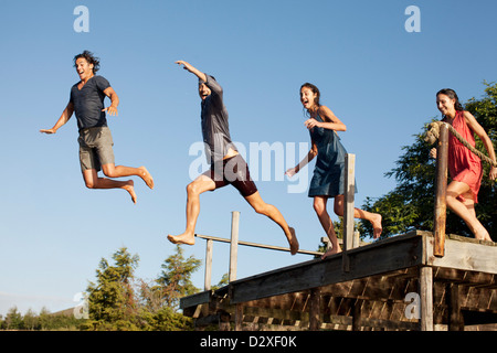 Enthusiastic friends Jumping off dock Banque D'Images