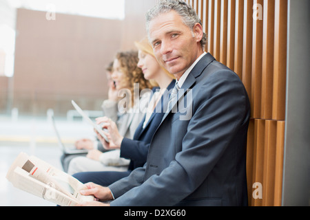 Portrait of businessman reading newspaper with co-workers in background Banque D'Images