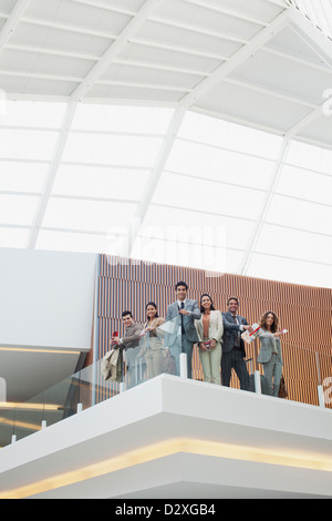 Portrait of smiling business people à rampe en verre de balcon in modern office Banque D'Images