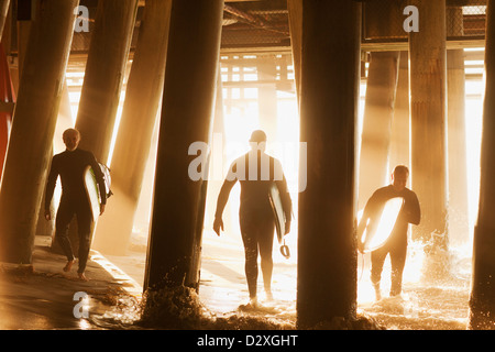 Surfers carrying boards sous pier Banque D'Images