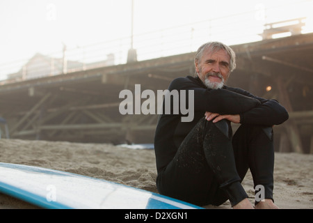 Plus surfer assis avec board on beach Banque D'Images