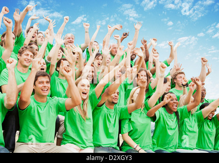 Foule en vert t-shirts cheering with arms raised Banque D'Images