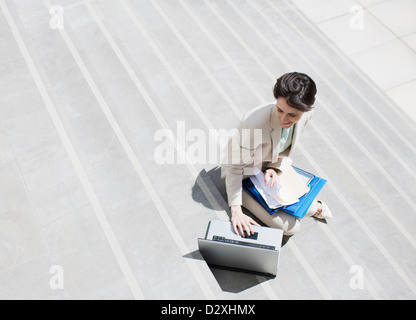 Businesswoman with paperwork using laptop on étapes urbaines Banque D'Images