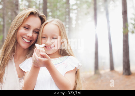 Smiling mother and daughter holding butterfly in woods Banque D'Images