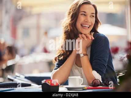 Smiling woman drinking coffee at sidewalk cafe Banque D'Images