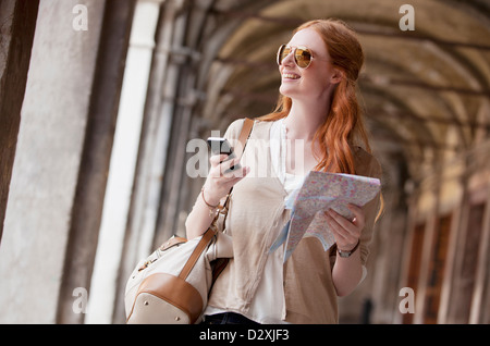 Smiling woman holding cell phone et carte in corridor Banque D'Images