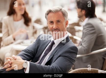 Portrait of smiling businessman at sidewalk cafe avec des collègues de travail en arrière-plan Banque D'Images