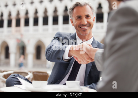 Smiling businessmen shaking hands at sidewalk cafe Banque D'Images