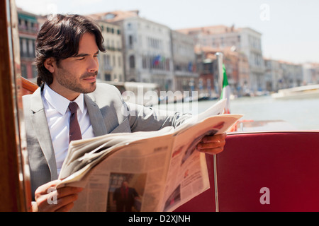 Businessman reading newspaper on boat in Venice Banque D'Images