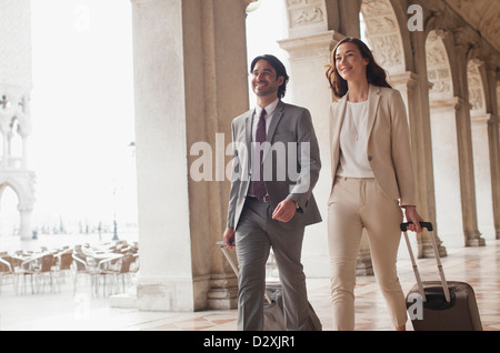 Smiling businessman and businesswoman pulling valises dans le couloir Banque D'Images