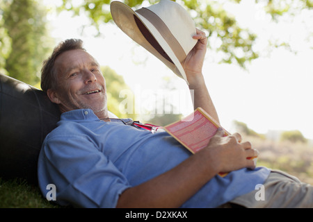 Portrait of smiling man laying on grass avec réserve et hat Banque D'Images
