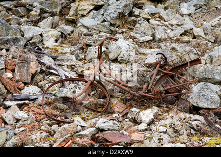 Un vieux vélo rouillé orange en couleur fixe sur les décombres de bâtiments détruits dans les ruines du village d'Oradour-sur-Glane. Banque D'Images