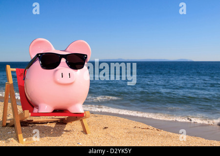 Pink piggy bank sur une plage dans une chaise portant des lunettes avec un sable doré et de l'océan bleu ciel bleu vif Banque D'Images