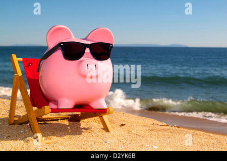 Pink piggy bank sur une plage dans une chaise portant des lunettes avec un sable doré et de l'océan bleu ciel bleu vif Banque D'Images