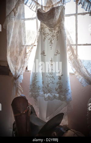 Une robe de mariage est suspendu devant une fenêtre, une selle est en dessous de la création d'un cadre de style old west Banque D'Images