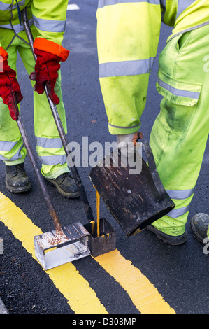 Les travailleurs de la route double peinture lignes jaunes le marquage routier sur une route, UK Banque D'Images