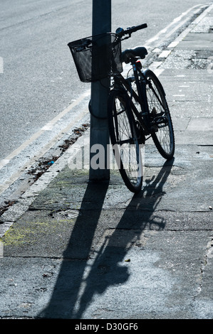 Un vélo appuyé contre un lampadaire à Cambridge UK se découpant dans la lumière du soleil forte Banque D'Images