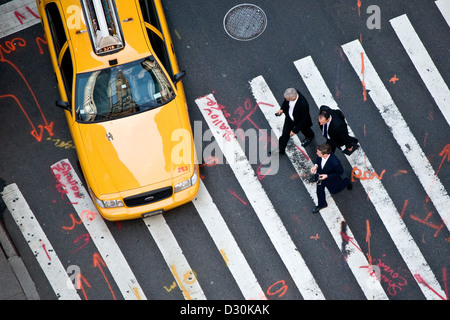 Hommes d'traverser la rue en face d'un taxi à Midtown Manhattan. Marquages sur la rue ressemblent à des notes de retouche. Banque D'Images