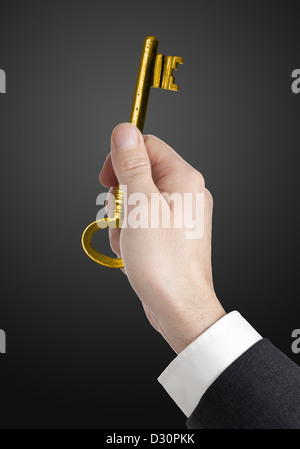 Main tenant la clé de la réussite d'or sur fond noir Banque D'Images