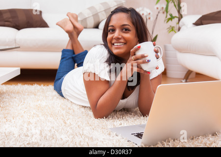 Les jeunes indiens heureux couché sur le plancher femme utilisant un ordinateur portable Banque D'Images