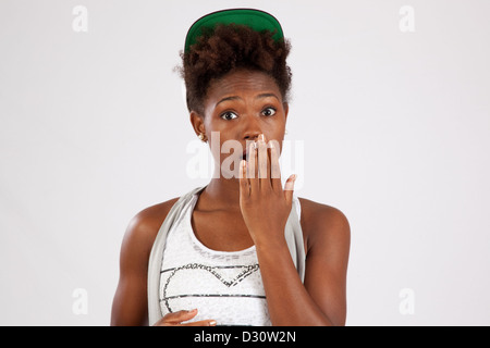 Jolie femme noire dans une casquette de baseball, tenant sa main sur sa bouche sous le choc et la surprise blanc regardant la caméra Banque D'Images