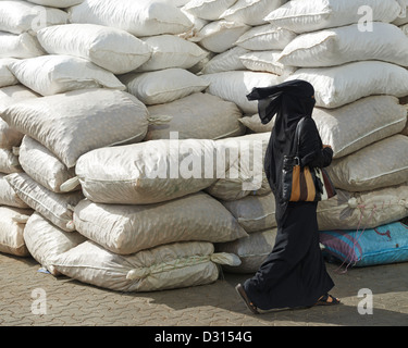 Une femme musulmane marche par d'énormes sacs de marchandises à Dubaï Banque D'Images