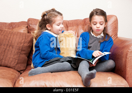 Les jeunes sœurs en uniforme de l'école primaire la lecture d'un livre ensemble. Banque D'Images