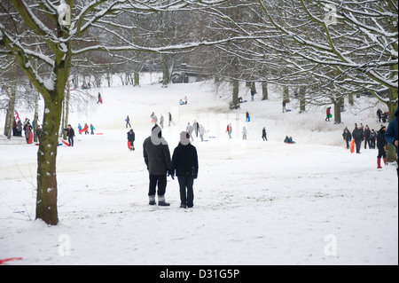 Un grand nombre de personnes de la luge ou de la luge dans un paysage couvert de neige avec deux adultes à l'avant-plan se tenant la main. Banque D'Images