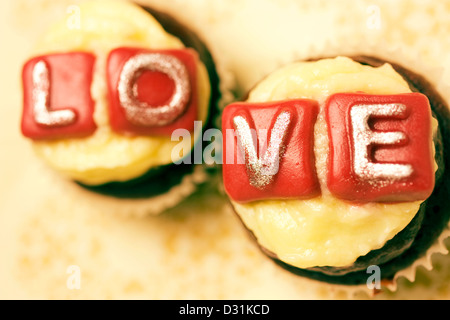 Deux petits gâteaux à thème la Saint-Valentin avec amour écrit sur eux. Red Velvet cupcake au fromage fondant l'écimage et l'alphabet Banque D'Images