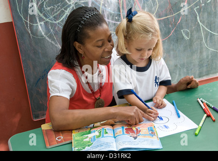 L'encadrement de l'enseignant la fille à attirer et reconnaît les formes à l'extérieur de la région de sunny ecole maternelle playschool Banque D'Images