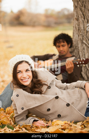 L'homme qui joue de la guitare pour l'amie dans les feuilles d'automne Banque D'Images