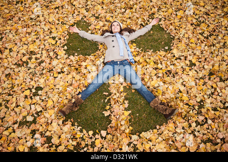 Caucasian woman faire ange dans les feuilles d'automne Banque D'Images