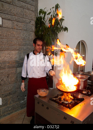 L'huile chaude sur une poêle à frire éclate en flammes tandis que le chef du restaurant prépare un repas sur une cuisinière à gaz extérieure. Village de Torba, péninsule de Bodrum, Turquie. Banque D'Images