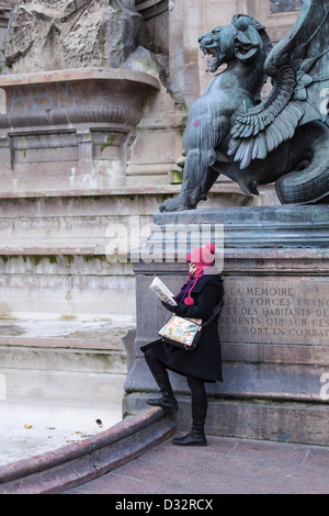 Lecture d'une fille par temps froid sous un dragon (par Henri Alfred Jacquemart) de la Fontaine Saint-Michel, Paris, France Banque D'Images