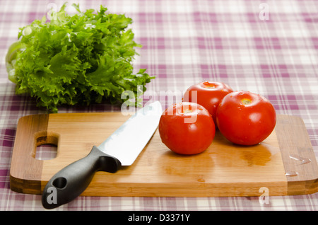 Les tomates et la laitue sur table avec planche à découper et couteau. Des ingrédients frais et sains, prête à être traitée à l'alimentation. Banque D'Images