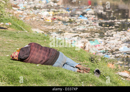 Un homme dormant sur les rives de la rivière Bishnumati fonctionnant grâce à Katmandou au Népal. Banque D'Images