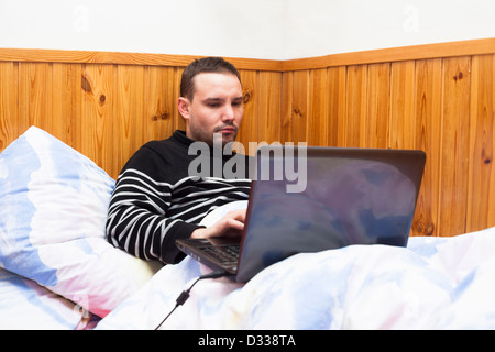 Jeune homme au lit et à l'aide d'ordinateur portable. Banque D'Images