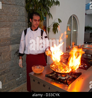 L'huile chaude sur une poêle à frire éclate en flammes tandis que le chef du restaurant prépare un repas sur une cuisinière à gaz extérieure. Village de Torba, péninsule de Bodrum, Turquie. Banque D'Images