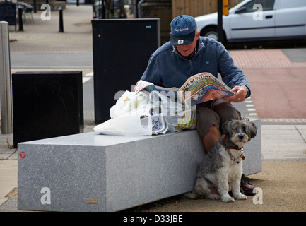 Homme assis sur le siège avec des sacs d'épicerie lisant le journal Sunday Times avec le chien assis patiemment attendant Cowes île de Wight, Hampshire, Royaume-Uni Banque D'Images