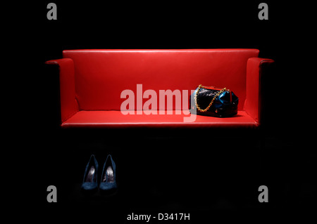 Canapé en cuir rouge avec sac à main et chaussures pour femmes. Banque D'Images
