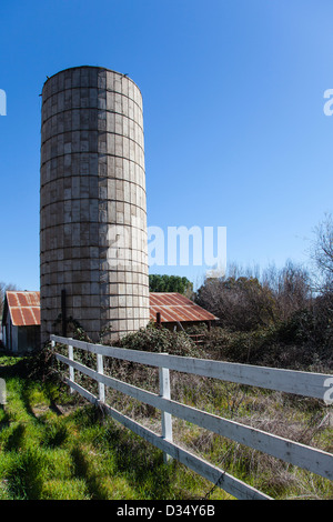 Un silo en béton et métal rouillé toit d'un bâtiment de ferme à l'arrière-plan blanc et clôture en premier plan dans la région de Santa Ynez, en Californie. Banque D'Images