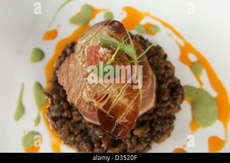 Thon poêlé avec foie gras poêlé, chutney de tomates et lentilles du Puy aux épices servi sur une plaque blanche. Banque D'Images