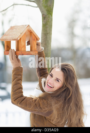 Smiling young woman hanging mangeoire pour oiseaux sur l'arbre en hiver Banque D'Images
