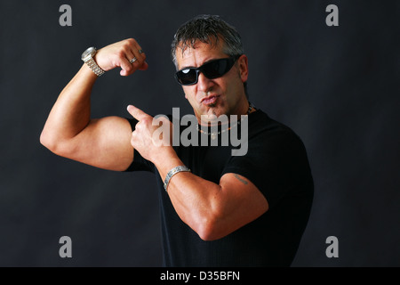 Dur à cuire avec des lunettes noires, pourrait être pénale, montrant son gros muscle biceps a l'intimidation studio shot sur fond noir. Banque D'Images