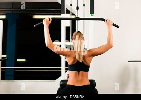 Belle femme faisant tirer-se lève sur une machine dans la salle de sport Banque D'Images