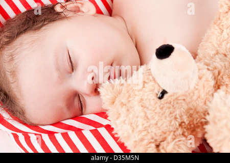 Mignon petit bébé à dormir sur le rouge et blanc oreiller avec ours Banque D'Images